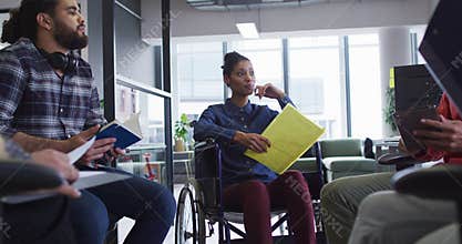 Mixed race businesswoman sitting in wheelchair discussing with diverse group of colleagues