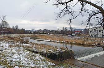 Ultra wide shot of white snow fall spread over grass by the river with small water fall in country side of South Poland during