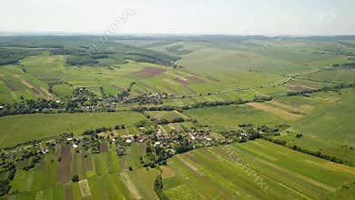 Aerial view of small village with small houses among green trees with farm fields and distant forest in summer.