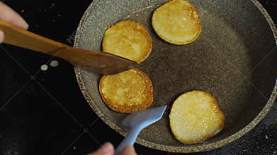 Women`s hands with their spatulas remove the cooked pancakes from the pan. Close-up