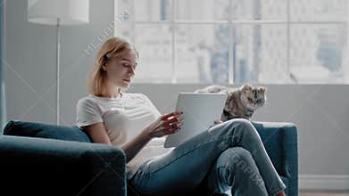 Woman with tablet rests near adorable cat on azure couch