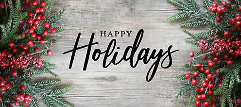 Happy Holidays Text with Holiday Evergreen Branches and Red Berries Frame Over Rustic Wooden Background