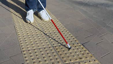 Legs of blind person searching special tactile tiles using cane. Blind man walking with a cane in the street