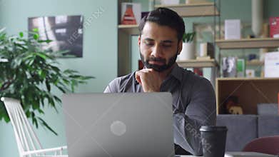 Bearded indian business man watching online webinar on laptop computer.