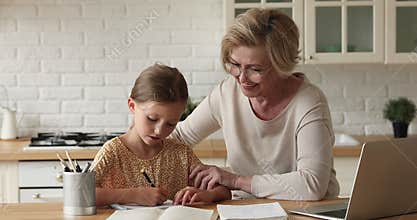 Loving grandmother helps to small granddaughter with homework at home