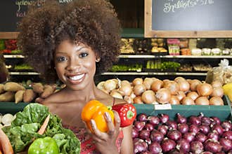 African American woman holding bell peppers and vegetables at supermarket