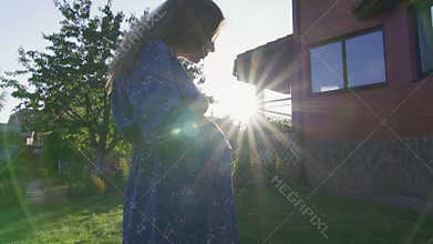 Beautiful pregnant woman enjoying fresh air at sunset rays on the backyard