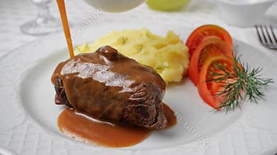 Chef hand pouring brown sauce on beef rouladen stuffed with mustard, onions, pickled cucumber and bacon.