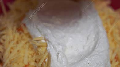 A person is spreading a white sauce on a cheese dish. The sauce is made from milk and is being spread with a spoon