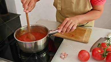 Woman cooking traditional Italian pasta sauce while wearing an apron in a home kitchen