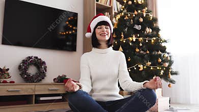 Young woman meditating by Christmas tree in cozy home setting