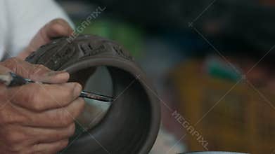 Person making black ceramic decorative pottery with tool