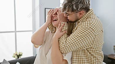 A man surprises a woman with a blindfold game in a cozy living room, expressing love and joy