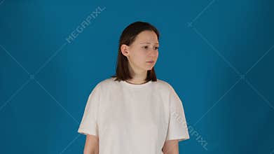 Pensive young woman in t-shirt stands on blue background