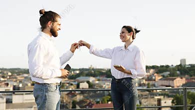 Real estate agent handing keys to new homeowner on rooftop