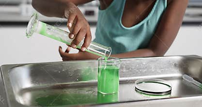 Child is tilting cylinder, pouring green liquid into beaker on tray making foam overflow for demo