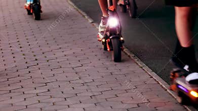 group of teenagers riding electric scooters through the park in the evening.