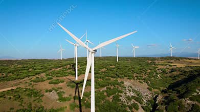erial drone footage of a wind farm with large wind turbines spinning over green fields under a clear blue sky. The video
