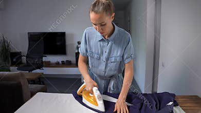 Middle-aged woman ironing a man's shirt in her living room. Domestic chore.