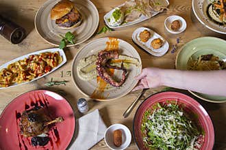 Human hand serving a plate over a variety of meat and fish meals. Buffet top view with a variety of food. Buffet, banquet,