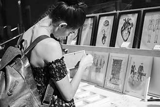 SÃ£o Paulo / SÃ£o Paulo / Brazil - 08 19 2018: Pretty exotic tropical woman choosing a drawing to buy at a market [B&W v]