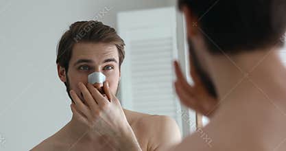 Smiling attractive young man applying nose strip cleansing pores blackheads