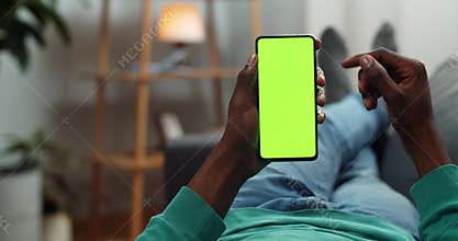 African american man scrolling mobile phone mock up screen while reading e book. Young man browsing net while lying on