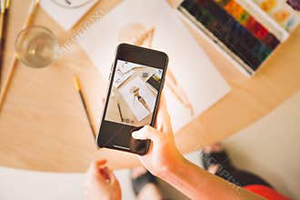 Illustrator girl blogger takes picture of watercolor drawing on phone. Photography for ad courses illustrations or blog