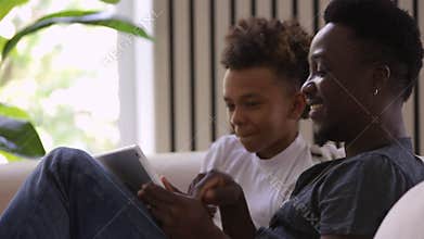 Dad and son laughing when looking at tablet screen Spbi. tell joke. bonding between father and teen