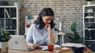 Worried manager using laptop and reading paper document working in office alone