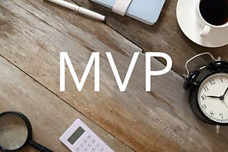 Top view of a cup of coffee,clock,notebook,pen,calculator,magnifying glass on wooden background written with MVP