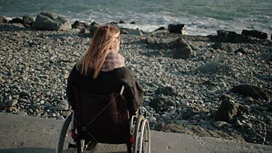 Woman with disabilities is sitting in invalid carriage and looking on sea