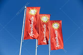 TOENISVORST, GERMANY - JUIN 28. 2019: Close up of red flags against blue sky with sun logo of Merkur Spielothek german gambling