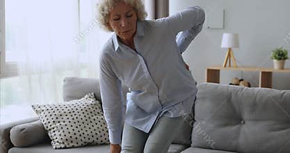 Upset senior woman feel back ache getting up from sofa