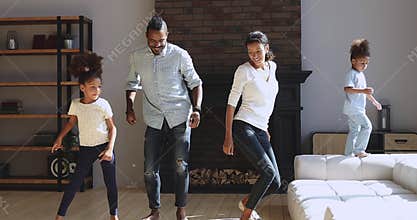 Joyful active african american family dancing jumping in living room