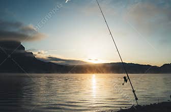 Fishery relax concept, outline fishing rod at sunrise sunlight, hobby sport on mist evening lake, catch fish