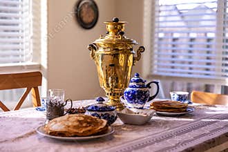 Traditional setup for Russian tea ceremony with samovar, bliny pancakes, teapot, sugar bowl and cups