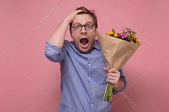 Young caucasian man in glasses having surprised face with flowers for his girlfriend