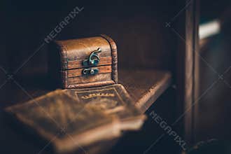 An old chest on a wooden shelf, in leather upholstery, in the foreground books are out of focus
