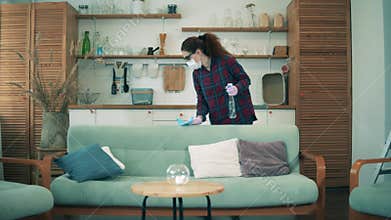 COVID-19 lockdown concept. A woman is sanitizing furniture while wearing a face mask