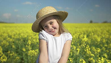 Little beautiful happy girl smiles in a yellow field hides behind a bouquet of yellow flowers