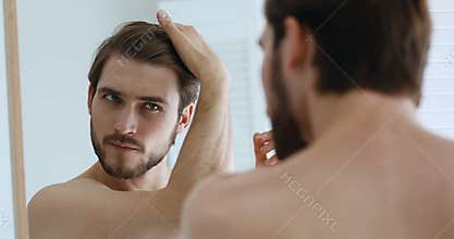 Young serious handsome european man assessing hair condition.