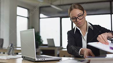 Young woman secretly reading magazine in office, lazy employee avoiding work