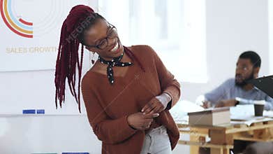 Happy young casual African woman boss in eyeglasses leading discussion, chatting to colleagues at modern light office.