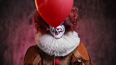Creepy clown releases a red ball and shows his face. Clown in a colorful makeup