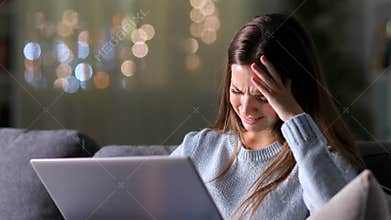 Sad woman reading bad news on laptop in the night