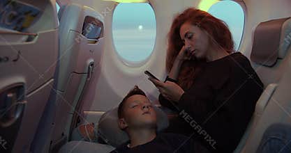 Boy sleeping on hands of mother while having flight in airplane.