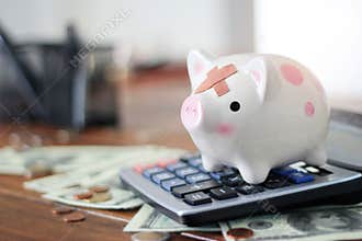 Abstract sick and injured piggy bank standing on calculator among money and coin on table in office. business financing accounting