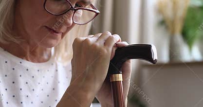 Upset old senior woman holding cane stick feeling sad, closeup