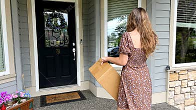 A teenager stands in a short summer dress against the backdrop of a private house in Canada, she holds a cardboard box